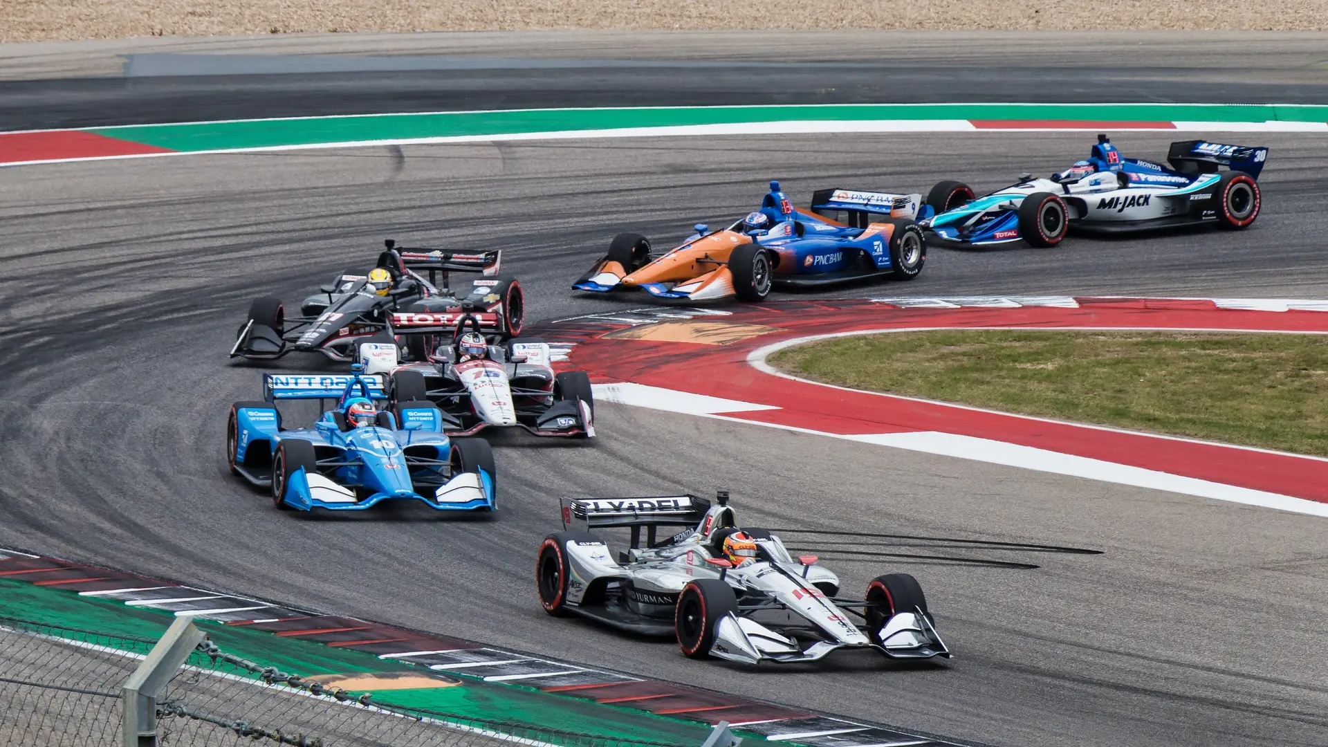 A pack of IndyCar Series cars racing through a corner in 2019