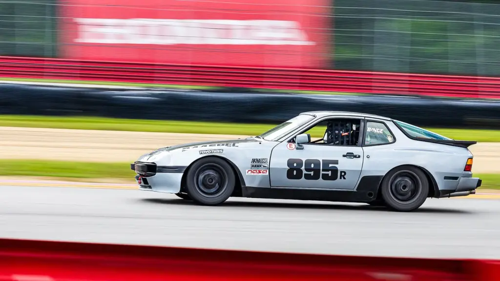 Silver Porsche 944 Spec race car at speed at Mid-Ohio